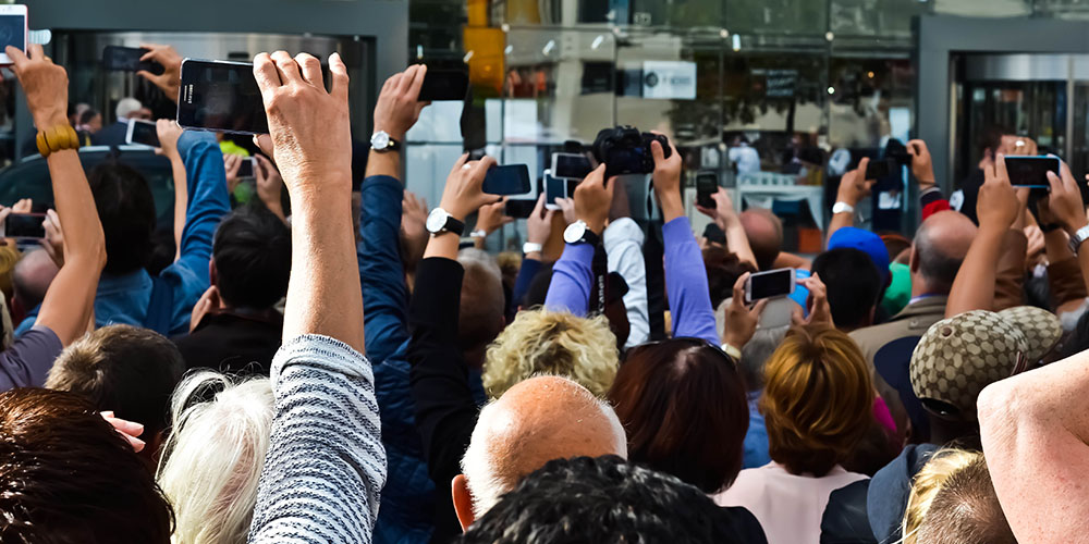 A crowd of people facing away from the camera hold their cameras up to take photos.
