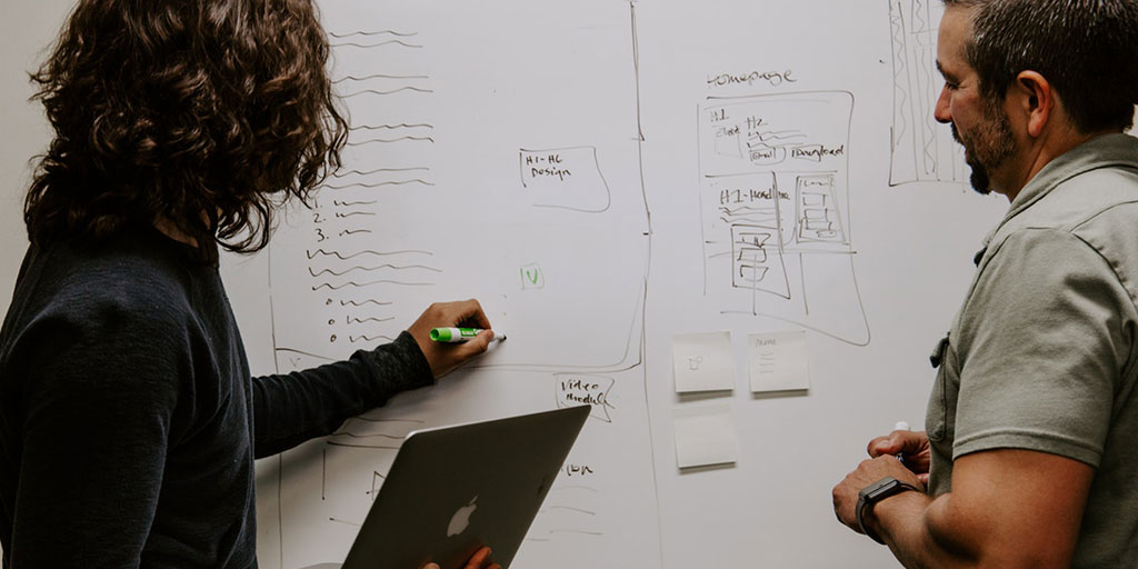 A man and women work at a whiteboard.