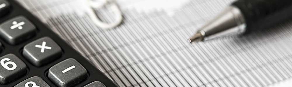 A close up of a pen resting on business paper. There is a calculator next to the pen.