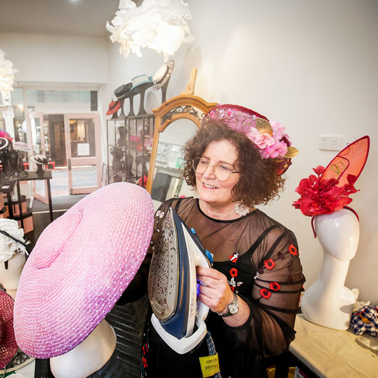 A woman working at Wendy Scully holding a pink header piece called a fascinator hat.