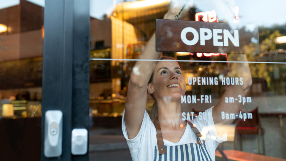 Happy business owner hanging an open sign at a cafe.