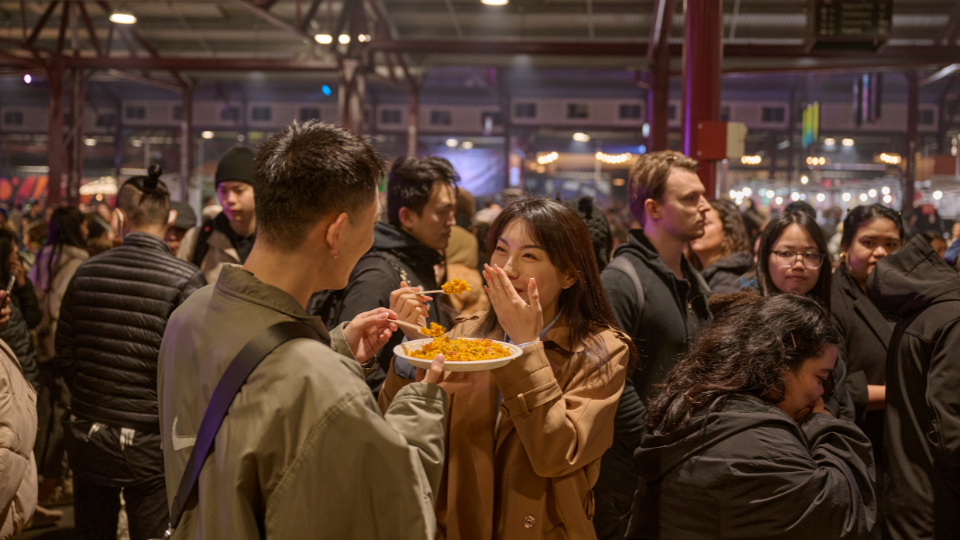 A man and woman eating food at a busy winter marketing in Melbourne.