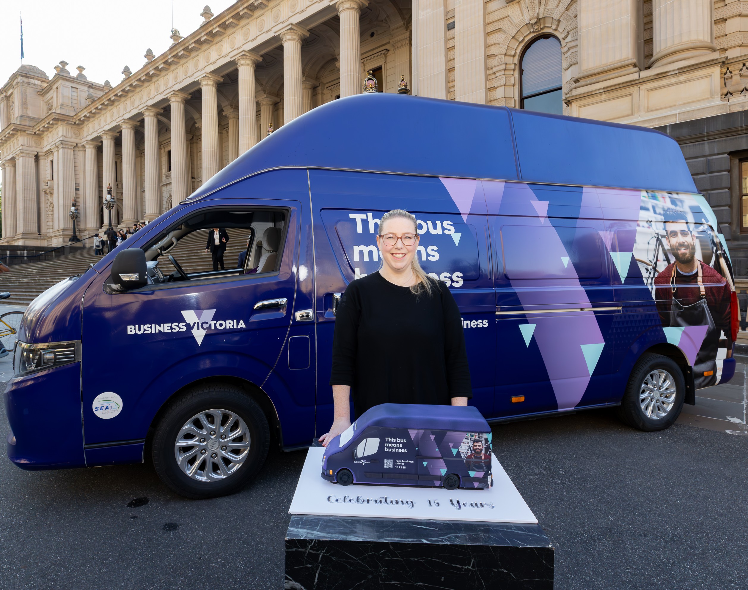 a woman with a bus -shaped cake in front of the bus