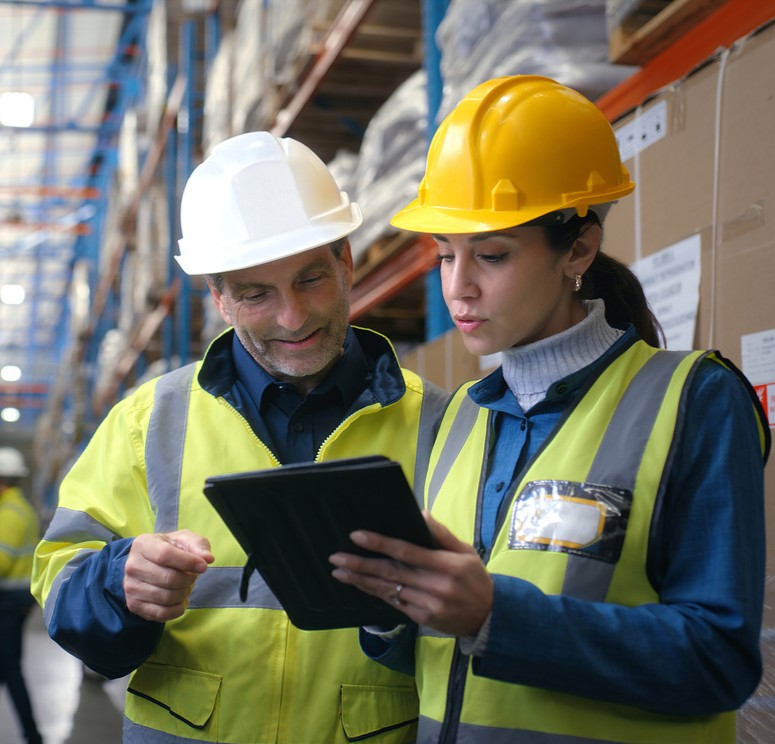 Two workers in high-visibility safety vests inspecting a warehouse loading dock floor.