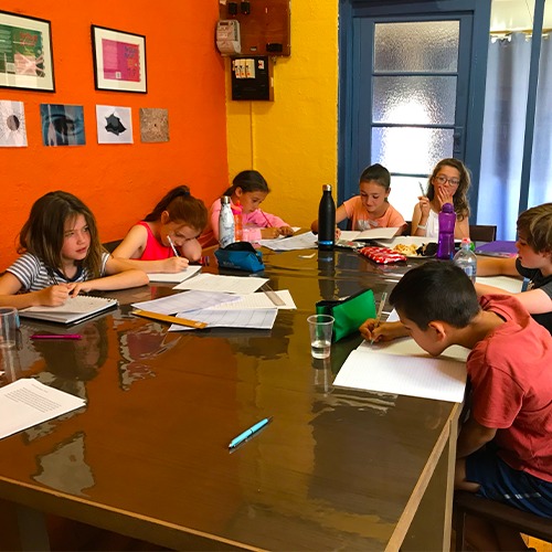 Several kids at a table writing in a notebook.