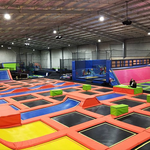 An indoor photo of Xtreme Bounce. There are many trampolines with colourful ramps and boxes spread out.