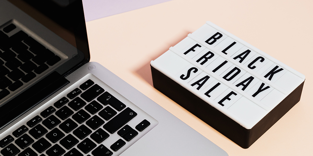 A black box with a white top sits on a table next to a laptop. On the top of the box, spelled out in black letters are the words, 'BLACK FRIDAY SALE