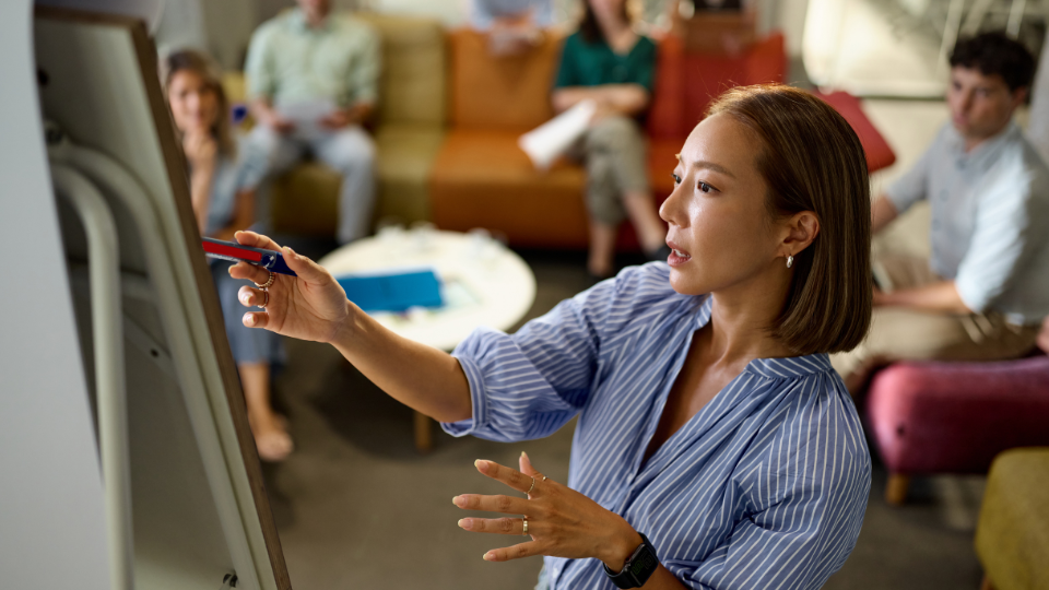 A woman with a pen, presenting to a group at work.