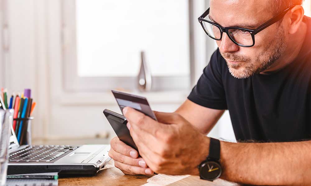 A man holding a credit card and a mobile phone.