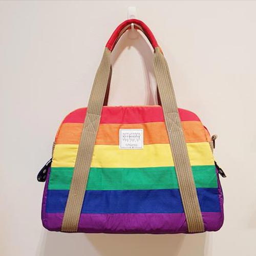 A rainbow coloured weekender bag hanging on a hook.