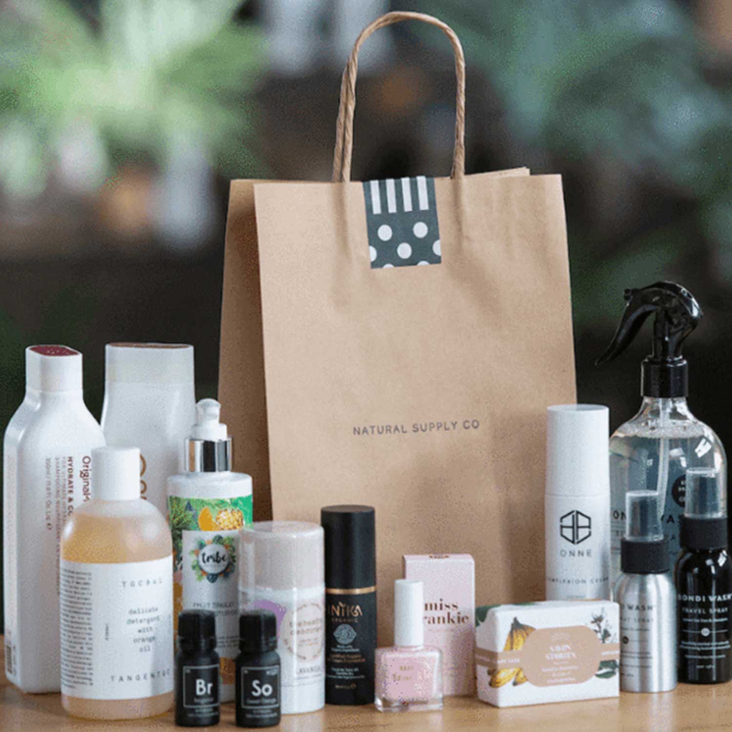 A table with a dozen Natural Supply skincare product. There is also a large paper bag with handles on the table.