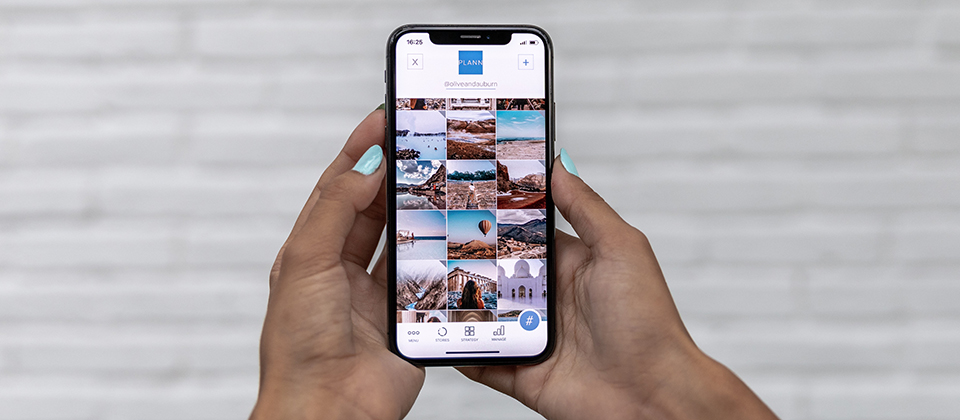 a woman’s hands with blue nail polish hold an iPhone showing a variety of travel photos in a grid