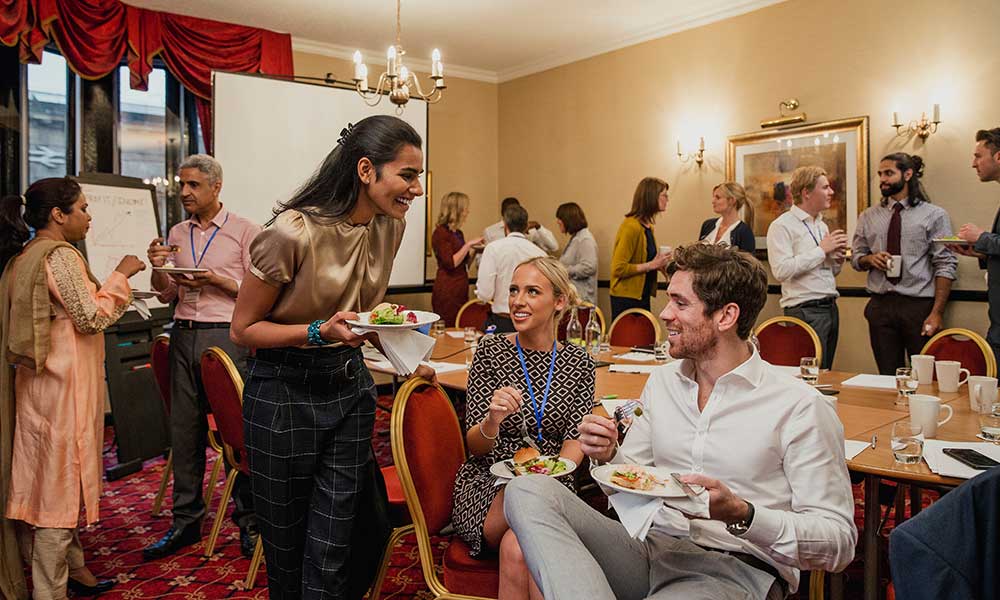 Smiling people eat and drink at a networking event.