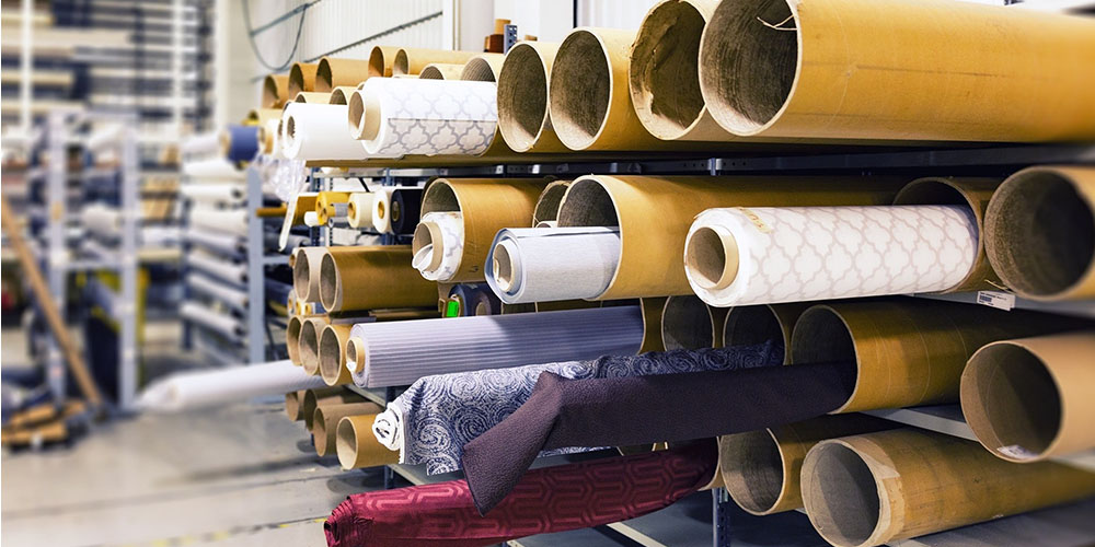 Rolls of patterned fabric sitting in large brown tubes in a rack in a warehouse.