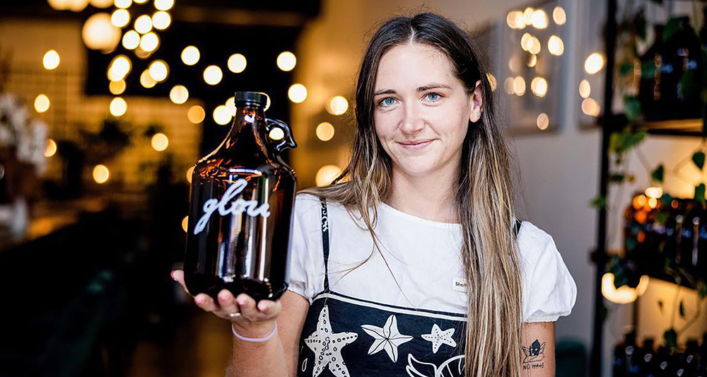 A young woman wearing a black and white dress is holding a re-usable wine bottle.