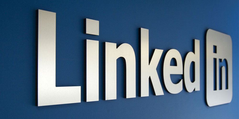 The LinkedIn logo as a silver sign on a blue wall.