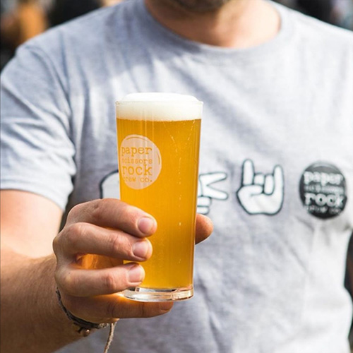 A man in a white t-shirt holding up a schooner of beer.