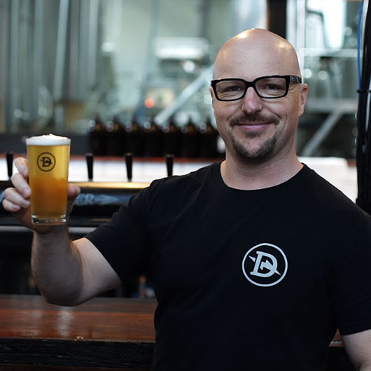 A man smiling at the camera holding a beer.