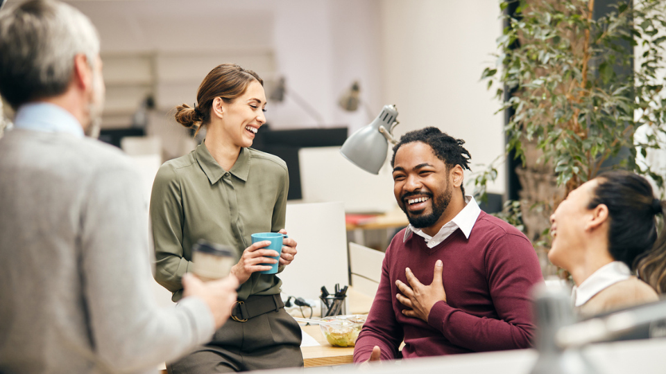 Four people in an office sitting at their desks, laughing on a coffee break.