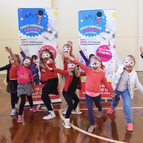 Seven kids posing with their arms out like wings. All of them are wearing white masks with the Disco Karaoke Parties banner behind them.