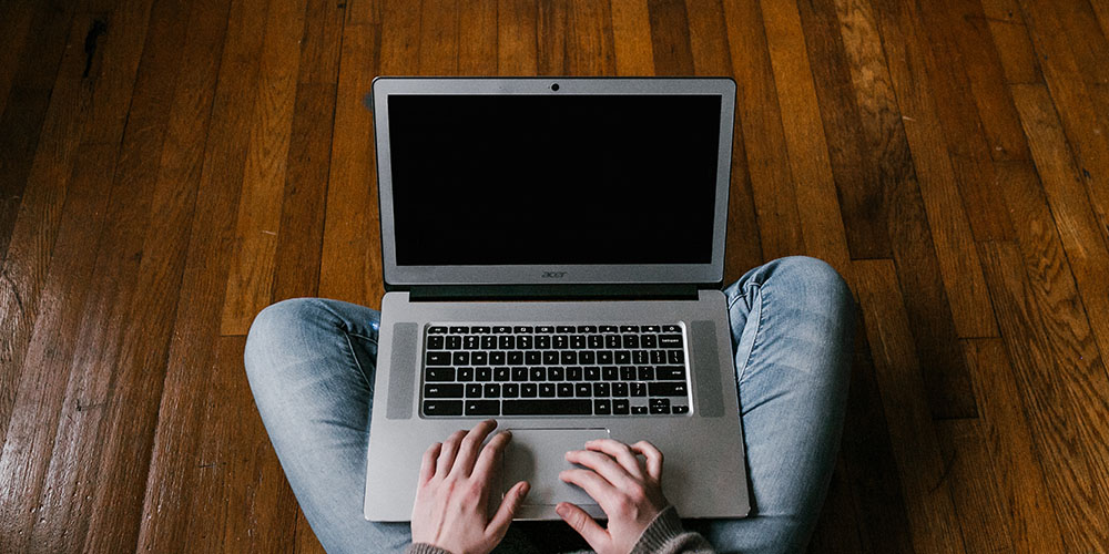 From a point-of-view perspective we see a woman’s hands as she works on a laptop that is balanced on her crossed legs. 