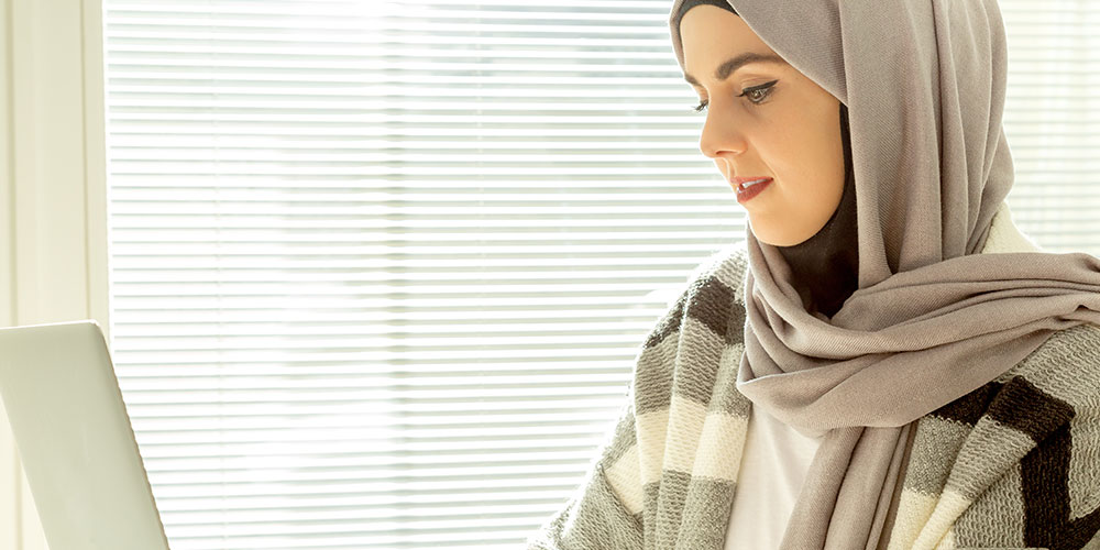 A woman wearing a hijab uses her laptop.