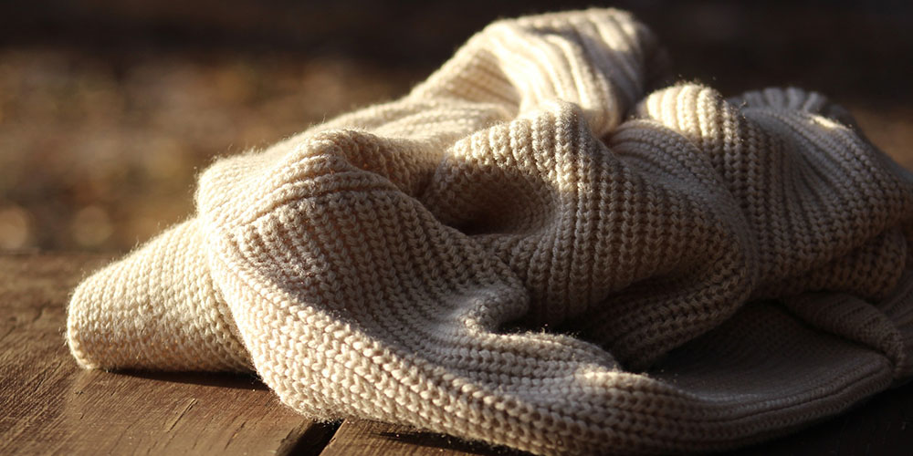 An off-white woollen jumper on a wooden tabletop.