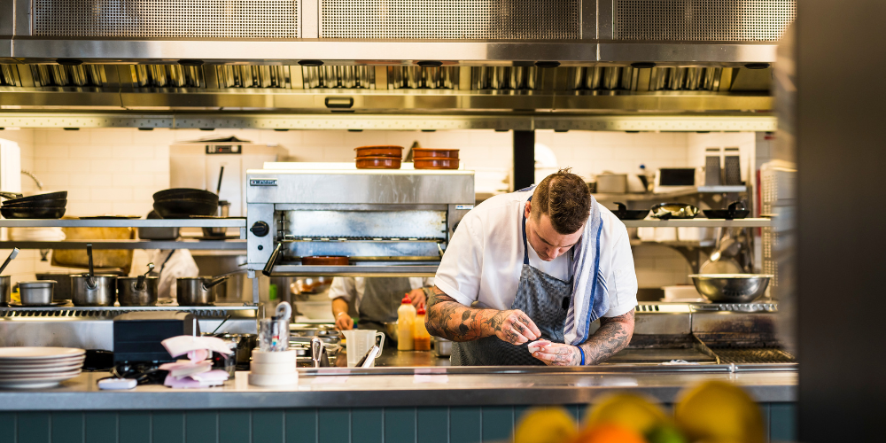 A chef in a kitchen at the service counter plating up food.