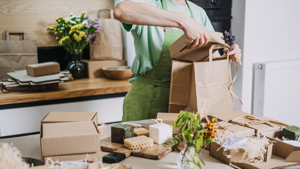 A person in an apron using cardboard to package a product.