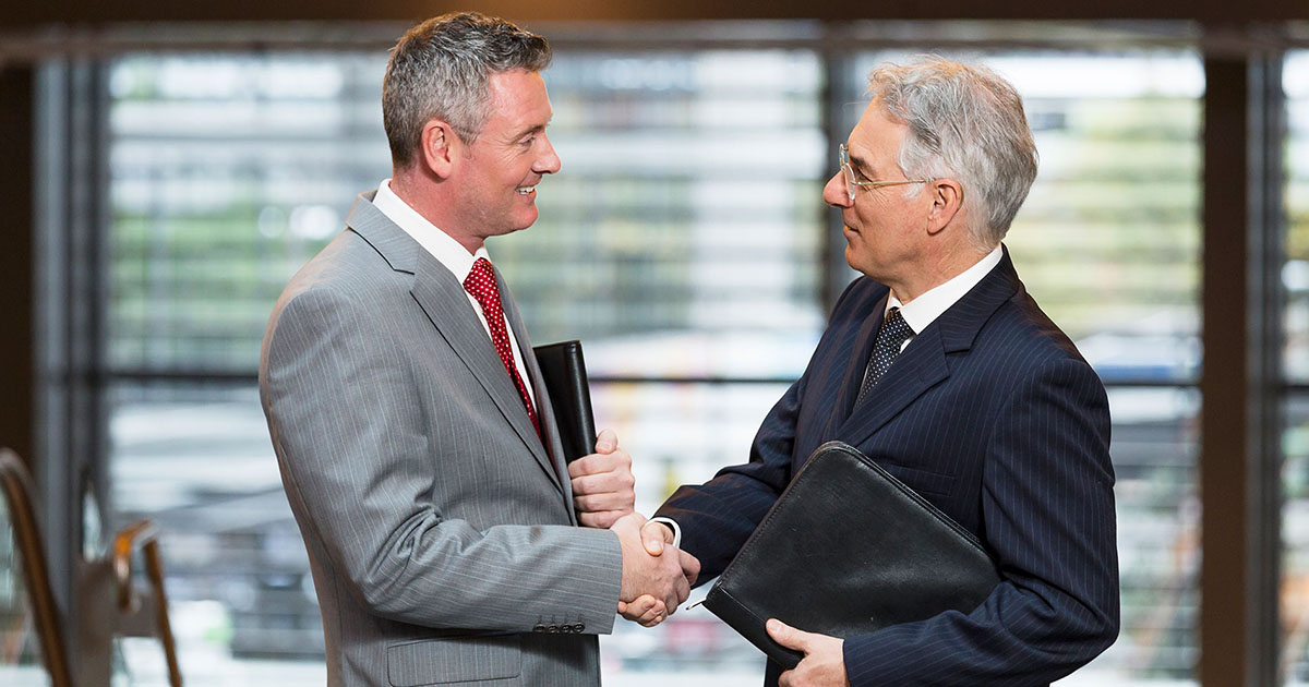 Two grey-haired men in suits shake hands