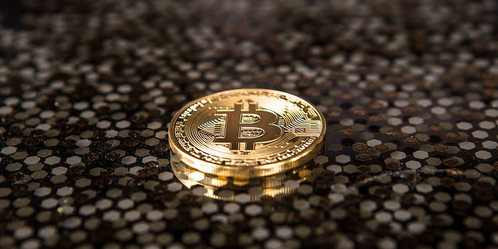 A gold bitcoin lying on a surface with a pattern of different coloured hexagons.