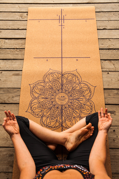 A top down view of a person sitting on a yoga mat with their legs crossed meditating. 