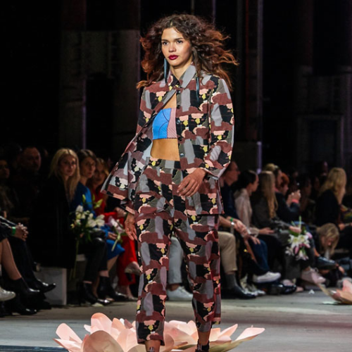 Model walking down a runway wearing a patterned suit during a fashion show.