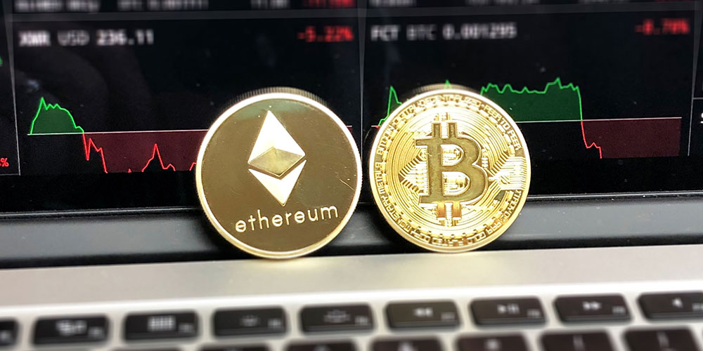 Gold Ethereum and Bitcoins sitting against a laptop screen showing market fluctuations.