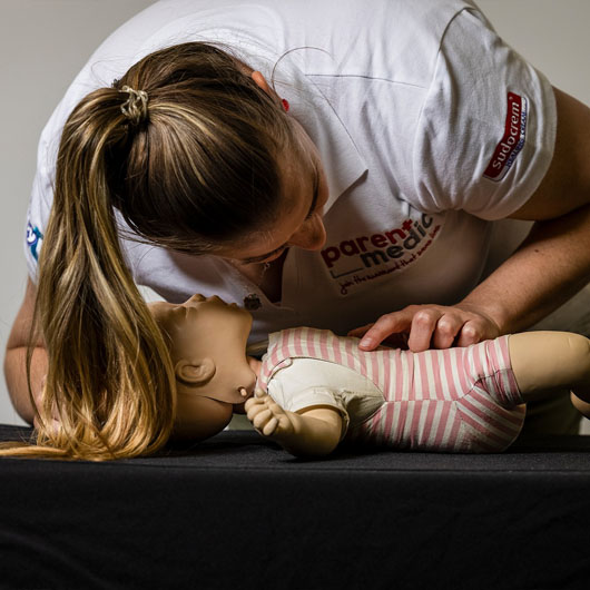 A worker at Parentmedic Victoria leaning over a training doll to check the airways of the mouth.