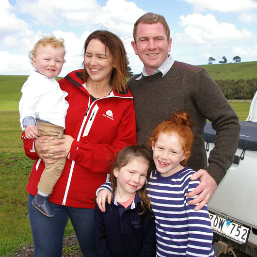A family of five standing in a grassy field smiling at the camera. The mum and dad have three daughters. 
