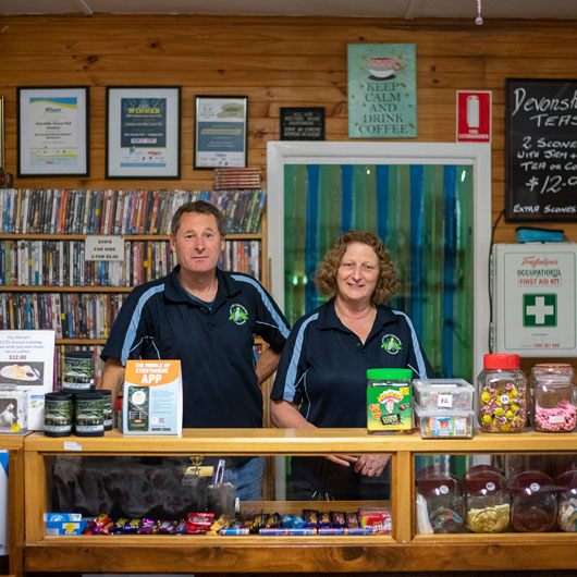 Two workers at Tarra Valley Caravan Park, standing behind the counter looking at the camera.