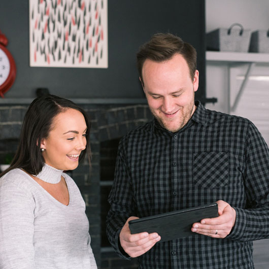 A man and a woman standing in an office. The man, on the right, is showing the woman something on his tablet.