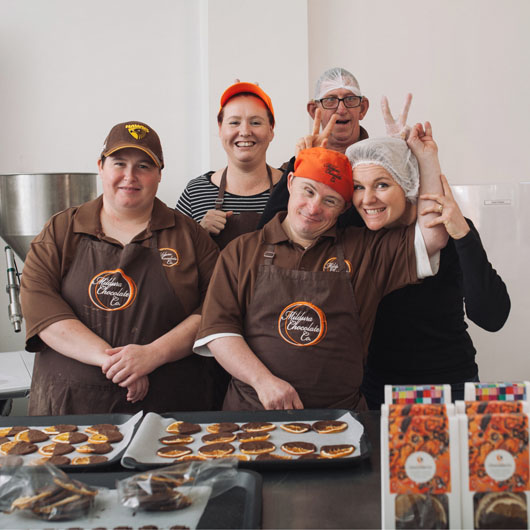 Five workers at Mildura Chocolate Company smiling at the camera. In front of them are biscuits.