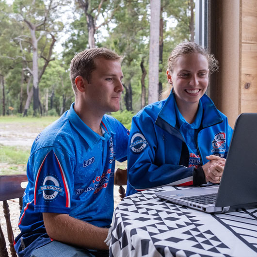 Two workers at Pureflow Cleaning sitting at a table looking at a laptop smiling.
