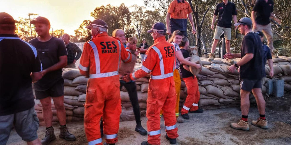 Several people in Castlemaine, Victoria building a sandbag wall to protect the small town from floods. There are people in civilian clothes and others in orange SES Rescue clothes.