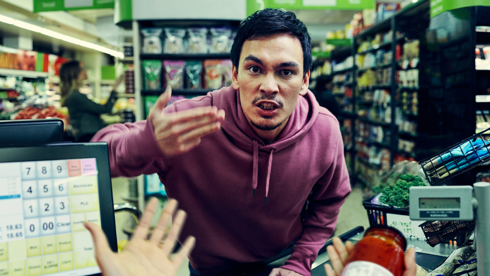 A man getting angry at someone working at the cashier in a supermarket.